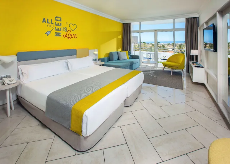 Double room with a yellow wall, a sofa and a balcony with views